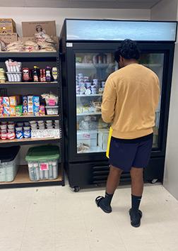 一名学生站在食品储藏室的玻璃门冷却器前.